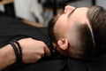 Cutting a gentlemans beard in a barbershop with a clipper. Shortening the length of the beard from the sides by the