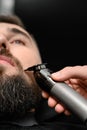 Cutting a gentlemans beard in a barbershop with a clipper. Shortening the length of the beard from the sides by the