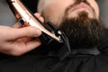 Cutting a gentlemans beard in a barbershop with a clipper. Shortening the length of the beard from the sides by the
