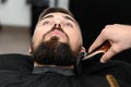 Cutting a gentlemans beard in a barbershop with a clipper. Shortening the length of the beard from the sides by the