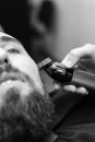 Cutting a gentlemans beard in a barbershop with a clipper. Shortening the length of the beard from the sides by the