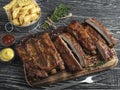 Cutting grilled pork ribs with sauce on a board, french fries, spices, wooden background Royalty Free Stock Photo