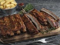 Cutting grilled pork ribs with sauce on a board, french fries, spices, wooden background Royalty Free Stock Photo