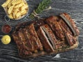 Cutting grilled pork ribs with sauce on a board, french fries, spices, wooden background Royalty Free Stock Photo