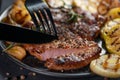 cutting with knife and fork grilled wagyu beef roast with vegetable on black plate