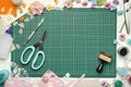 The cutting mat is surrounded by paper flowers, paper, tools and scrapbooking materials