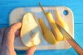 Cutting a pear with a hand with a knife on a wooden cutting board on a turquoise wooden table with long blue shadows