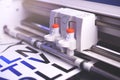 cutting plotter machine with adjustable blades makes adhesive lettering from black vinyl foil in bright light with blue highlights Royalty Free Stock Photo