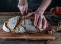 Cutting rustic loaf of sourdough bread by womans hand with a bread knife Royalty Free Stock Photo