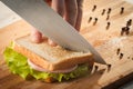 Cutting sandwich with bread, cheese, salad and ham with hands on wooden cutting board with knife Royalty Free Stock Photo