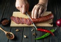 Cutting sausage on wooden cutting board at domestic kitchen by hands chef for a sandwich