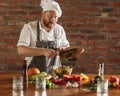 Young Caucasian red-bearded man, chef cooking fresh vegetable salad in cafe, restaurant kitchen. Concept of a correct Royalty Free Stock Photo