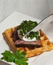 Cutting a steak, egg and waffle with an artisan knife square, white plate with a covering of chimichurri and a sprig of parsl