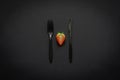 Cutting strawberry with fork and knife on dark background