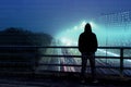 A cyber concept of numbers over layered over the top of a lone hooded figure looking at traffic from a bridge at night