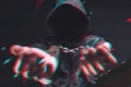 Cyber criminal arrest, unrecognizable hooded person with handcuffs, digitally enhanced glitch effect
