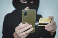 Cyber criminal in balaclava enters the information of a personal bank account. Credit card fraudulent scheme. Stealing cyber money