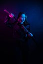 Cyber girl in a black leather jacket at dusk holds a katana. A woman in a club with a colored pink-blue light holds an Asian sword Royalty Free Stock Photo