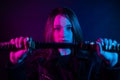 Cyber girl in a black leather jacket at dusk holds a katana. A woman in a club with a colored pink-blue light holds an Asian sword Royalty Free Stock Photo