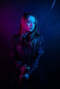 Cyber girl in a black leather jacket at dusk holds a katana. A woman in a club with a colored pink-blue light holds an Asian sword Royalty Free Stock Photo