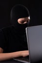 Cyber terrorist in a mask in a mask on a black background behind a laptop