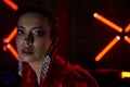 Cyberpunk close up of model wearing red bikers jacket sitting in leather sofa against neon