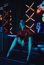 Cyberpunk shooting of model wearing red bikers jacket sitting in leather sofa against neon