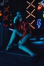 Cyberpunk shooting of model wearing red bikers jacket sitting in leather sofa against neon