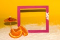 cyclamen color frame on yellow background with sand, creative summer concept, next to slice orange fruit Royalty Free Stock Photo