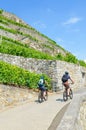 Cycling couple on path along green terraced vineyards in Swiss Lavaux wine region. The beautiful vineyard is located on slope by