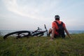 The cyclist with backpack, enjoys the view of the ocean, sits on the grass.