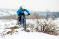 Cyclist in Blue Riding Mountain Bike on Rocky Winter Hill Covered with Snow. Extreme Sport and Enduro Biking Concept. Royalty Free Stock Photo
