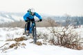 Cyclist in Blue Riding Mountain Bike on Rocky Winter Hill Covered with Snow. Extreme Sport and Enduro Biking Concept.