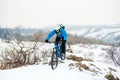 Cyclist in Blue Riding Mountain Bike on Rocky Winter Hill Covered with Snow. Extreme Sport and Enduro Biking Concept. Royalty Free Stock Photo
