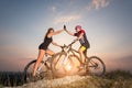 Cyclist couple with mountain bikes on the hill at sunset