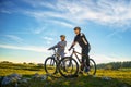 Cyclist couple with mountain bikes standing on the hill under the evening sky and enjoying bright sun at the sunset.