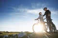 Cyclist couple with mountain bikes standing on the hill under the evening sky and enjoying bright sun at the sunset. Royalty Free Stock Photo