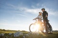 Cyclist couple with mountain bikes standing on the hill under the evening sky and enjoying bright sun at the sunset. Royalty Free Stock Photo