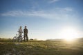 Cyclist couple with mountain bikes standing on the hill under the evening sky and enjoying bright sun at the sunset.