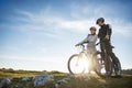 Cyclist couple with mountain bikes standing on the hill under the evening sky and enjoying bright sun at the sunset. Royalty Free Stock Photo