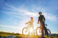 Cyclist couple with mountain bikes standing on the hill under the evening sky and enjoying bright sun at the sunset. Royalty Free Stock Photo