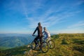 Cyclist couple with mountain bikes standing on the hill under the evening sky and enjoying bright sun at the sunset. Royalty Free Stock Photo