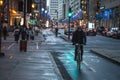 Cyclist, delivery courrier guy, standing with his bicycle on a bicycle lane in downtown center business district at night