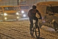 Cyclist while driving on a snow-covered road in the general flow of cars in the evening Royalty Free Stock Photo
