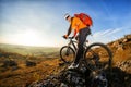 Cyclist in helmet and glasses on mountain bike stands on the precipice of hill under blue sky and sun. Wide angle view Royalty Free Stock Photo