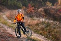 Cyclist in the orange jacket riding a bike on countryside road at the sunrise.