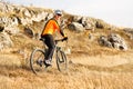 Cyclist in Orange Jacket Riding the Bike Rocky Hill. Extreme Sport Concept. Space for Text. Royalty Free Stock Photo