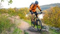 Cyclist in Orange Riding the Mountain Bike on the Autumn Rocky Trail. Extreme Sport and Enduro Biking Concept.