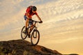 Cyclist in Red Riding the Bike Down the Rock at Sunset. Extreme Sport and Enduro Biking Concept.