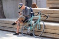 cyclist resting next to a bicycle on a city street